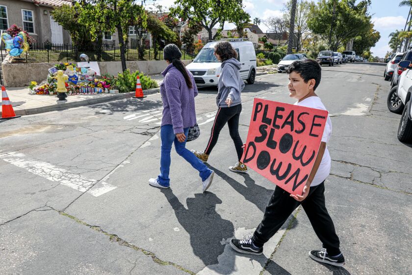 Kaiden Maldenado, 10, holds a sign that reads "please slow down" next to a memorial site where 6-year-old boy was killed on the intersection of Kensington Avenue and Biona Drive on Saturday, March 25, 2023.