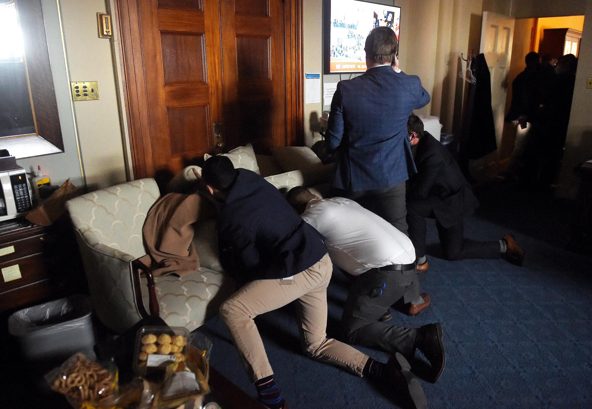 Two men push a couch in front of a door.