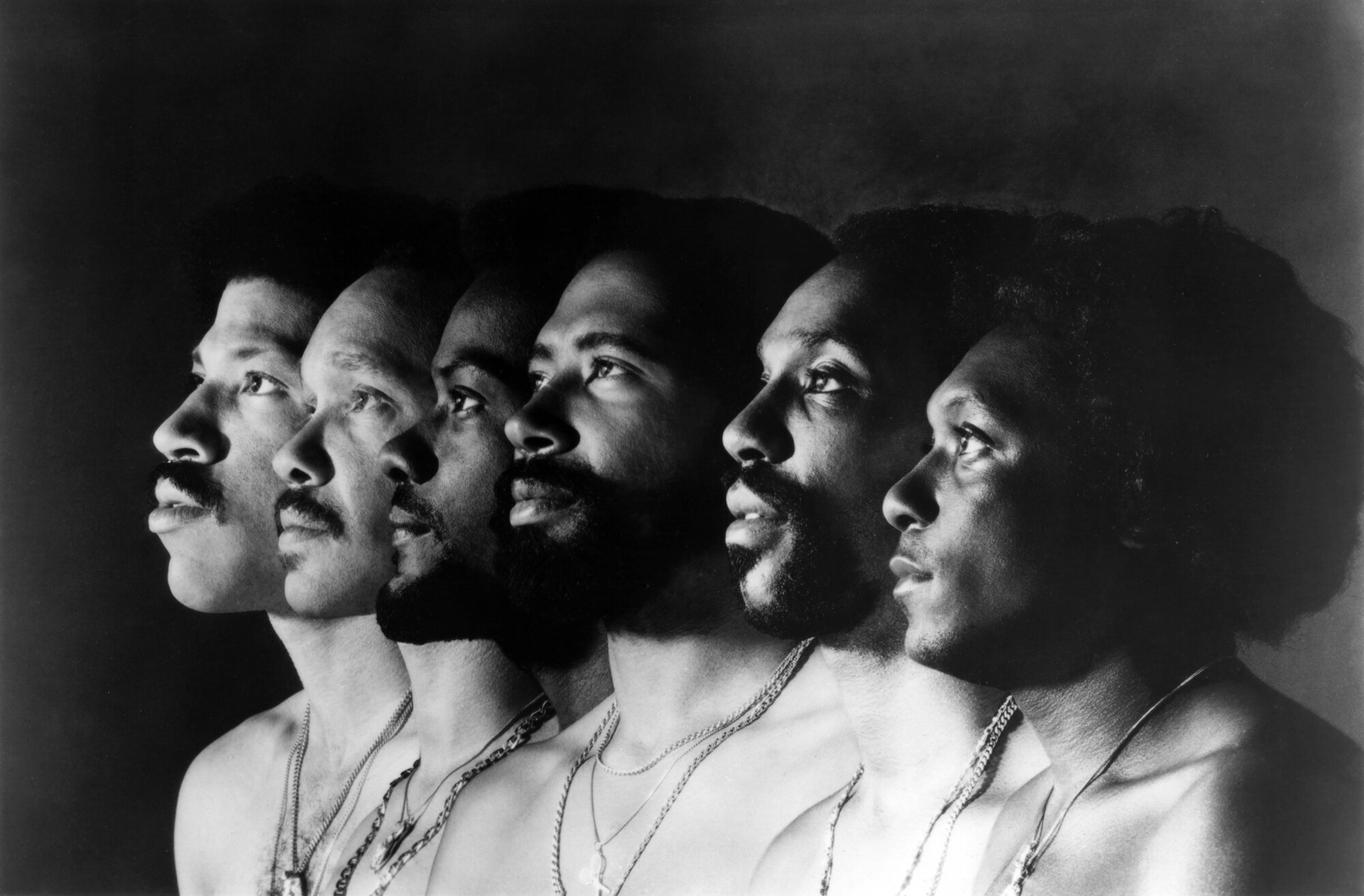 A profile view of Lionel Richie and the other Commodores, standing side by side 