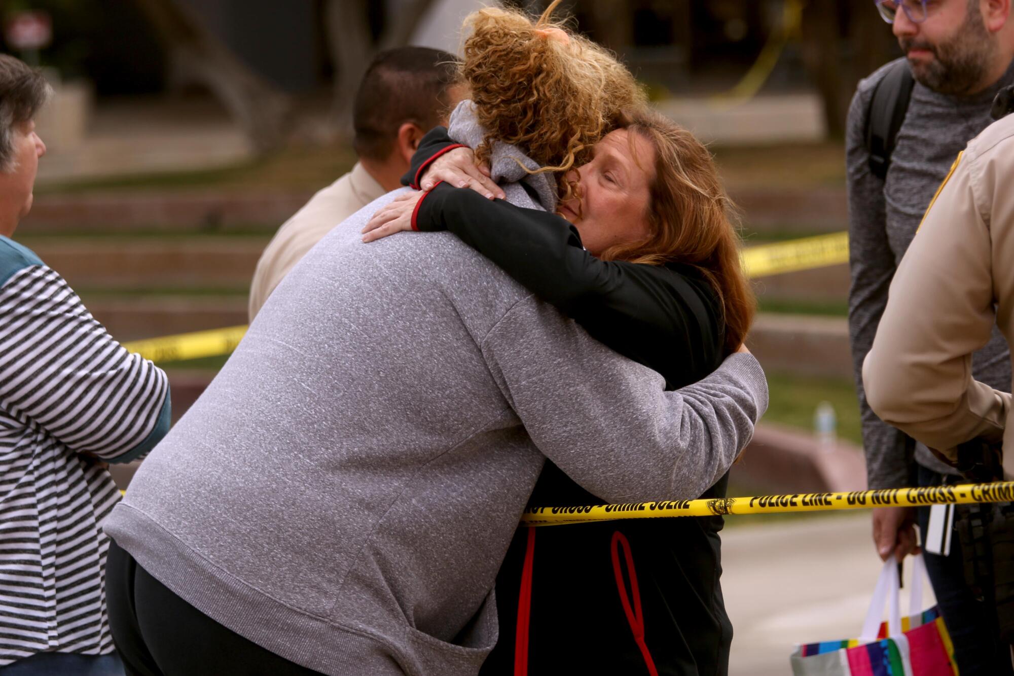 A student is hugged by a campus worker across yellow police tape. 