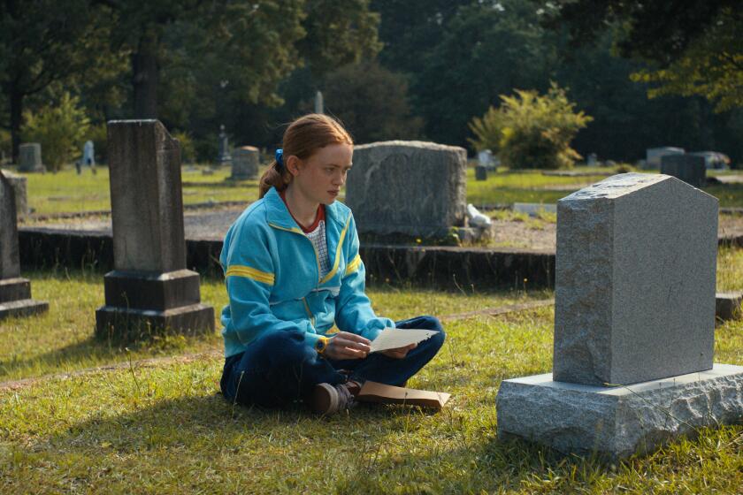 A teenage girl sits cross-legged on the ground in front of a tombstone