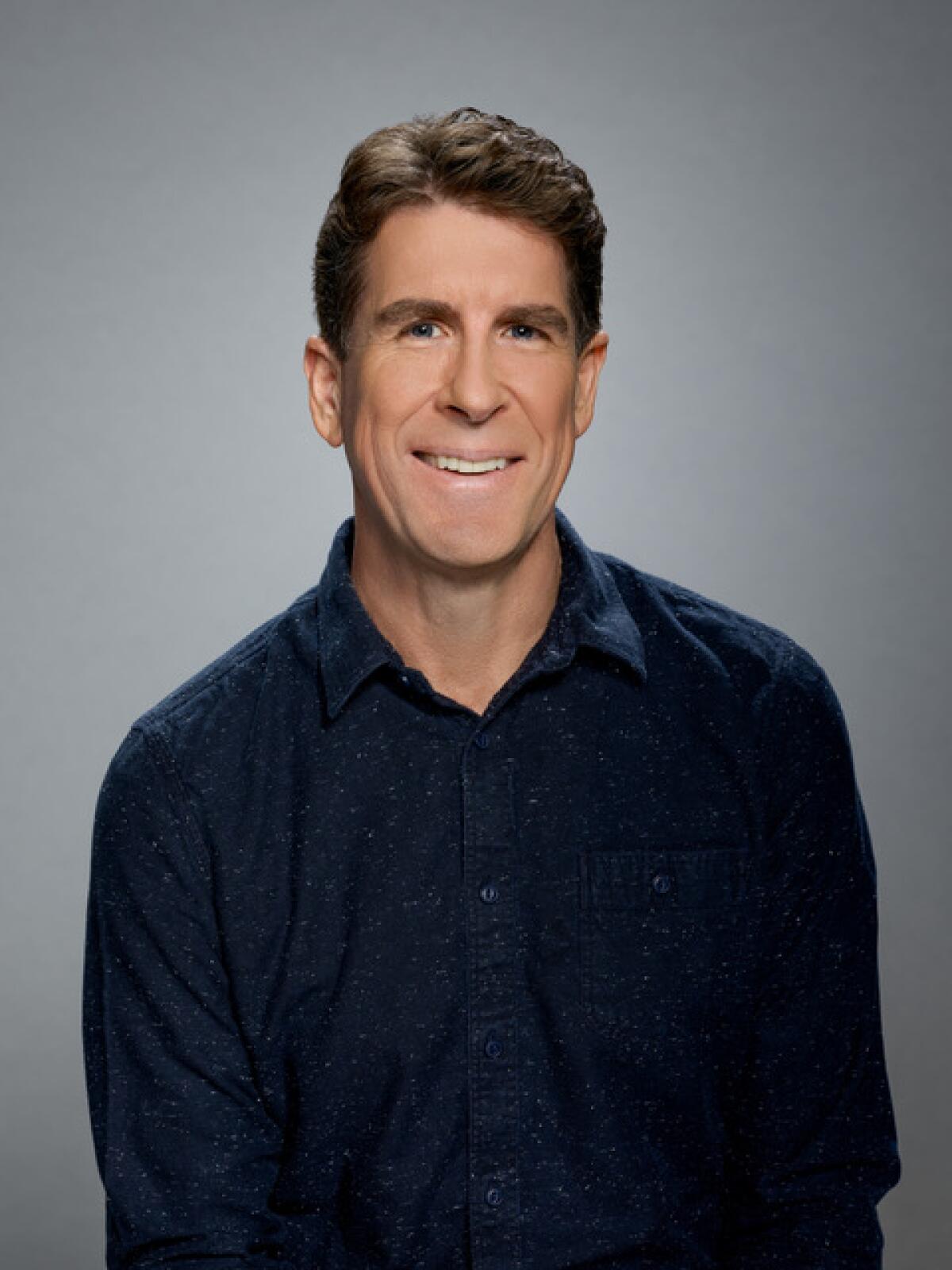 A smiling man in a dark blue button-down shirt, the Emmy-nominated composer of songs from a fake musical for "Schmigadoon!"