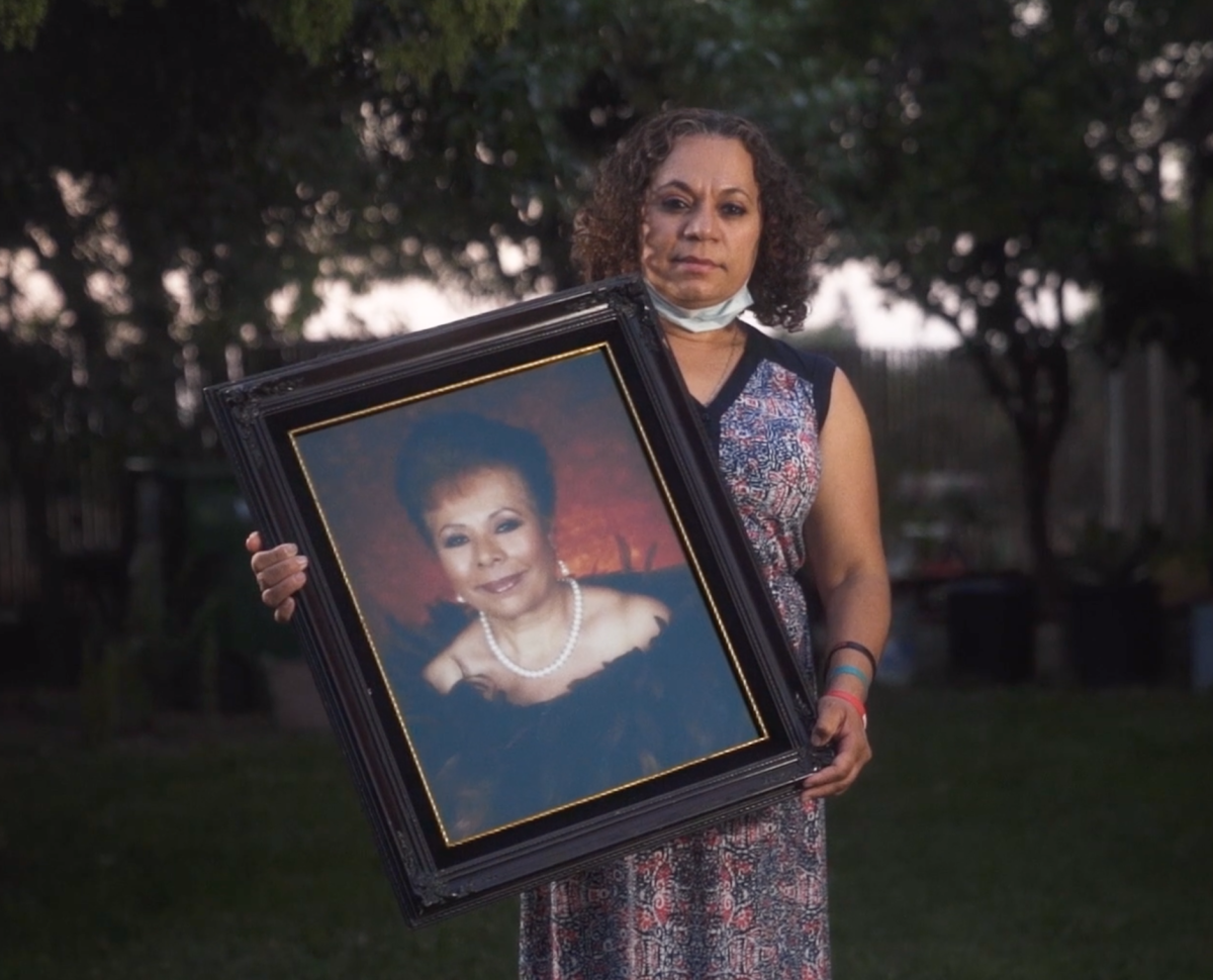 A woman holds a framed portrait of her mother.