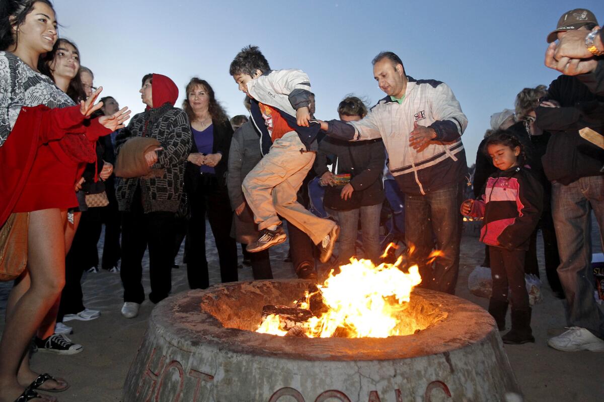 Kianoush Hamadani, center right, of Irvine, helps his son Cameron over a bonfire in celebration of the Persian New Year, known as Norooz, held at Corona del Mar State Beach.