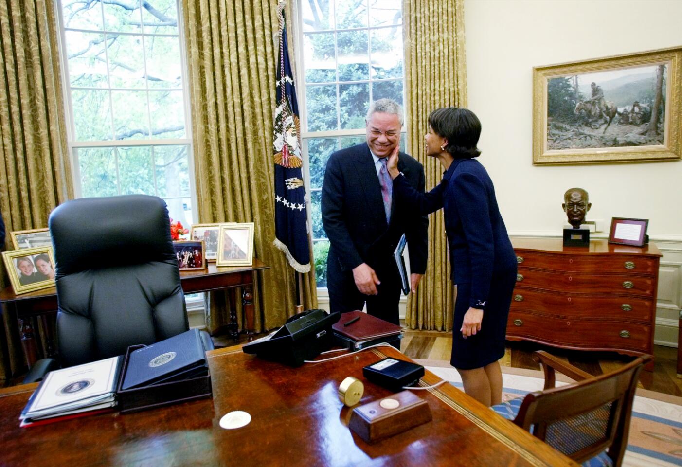 Secretary of State Colin Powell receives a pat on the cheek from Condoleezza Rice in an office.