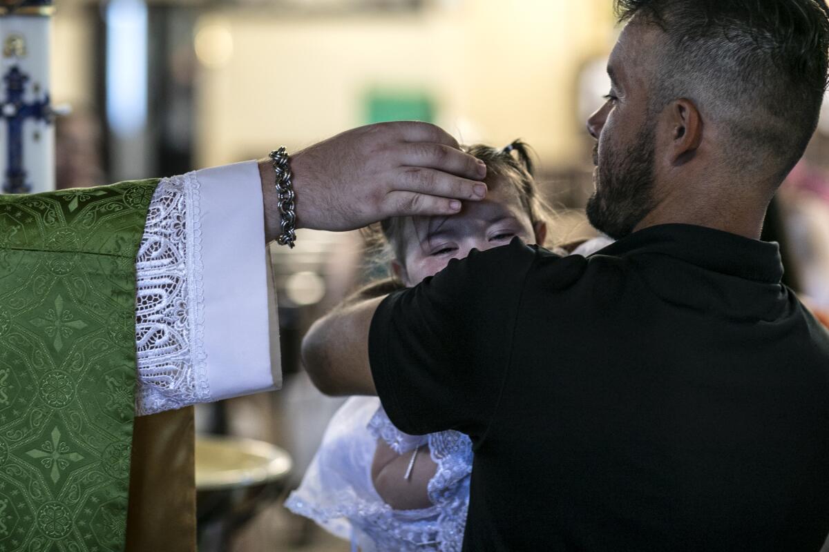 A father holds his daughter as she is baptized at a Catholic church in Sioux Falls, S.D.