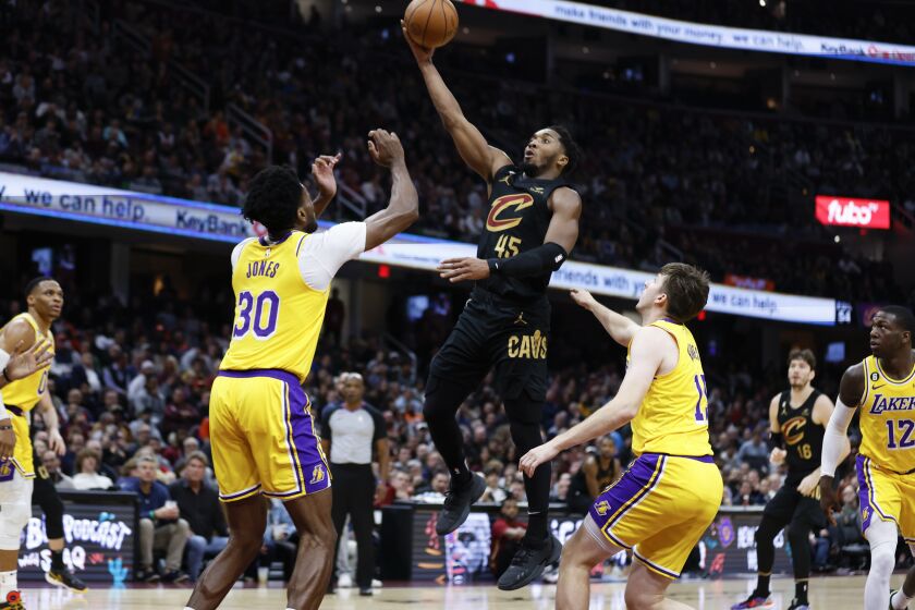 El base de los Cavaliers de Cleveland Donovan Mitchell lanza el balón sobre el pívot de los Lakers de Los Ángeles Damian Jones y el base Austin Reaves en el encuentro del martes 6 de diciembre del 2022. (AP Foto/Ron Schwane)