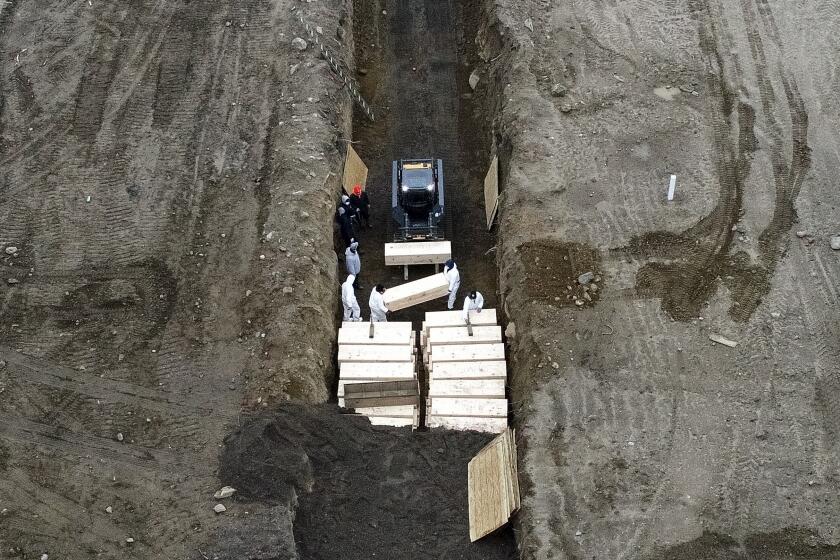 Workers wearing personal protective equipment bury bodies in a trench on Hart Island, Thursday, April 9, 2020, in the Bronx borough of New York. On Thursday, New York City's medical examiner confirmed that the city has shortened the amount of time it will hold on to remains to 14 days from 30 days before they will be transferred for temporary internment at a City Cemetery. Earlier in the week, Mayor Bill DeBlasio said that officials have explored the possibility of temporary burials on Hart Island, a strip of land in Long Island Sound that has long served as the city's potter's field. (AP Photo/John Minchillo)