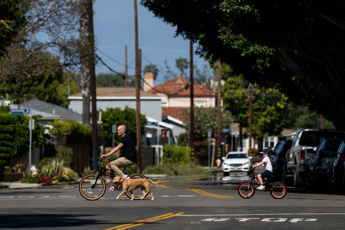 A man on a bike leads a dog as well as a child on a bike along Maxella Avenue in Los Angeles' Del Rey neighborhood. 