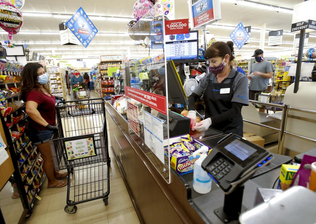 A shopper and a cashier at a grocery store both wear masks