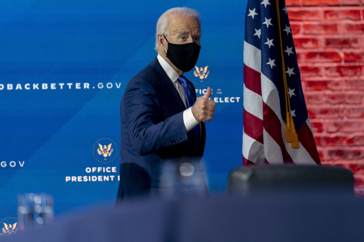 President-elect Joe Biden, wearing a face make, flashes a thumb up.