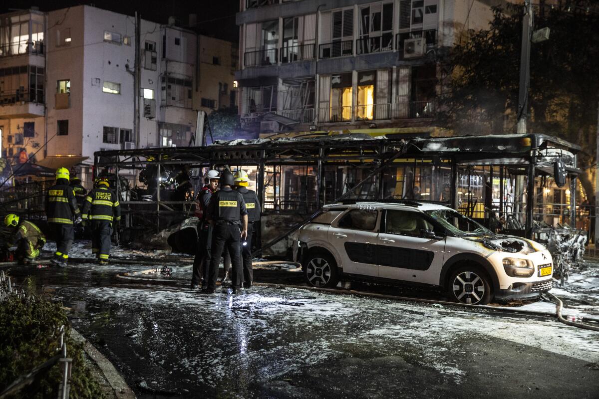 Firefighters gather near a car and a building struck by a rocket 