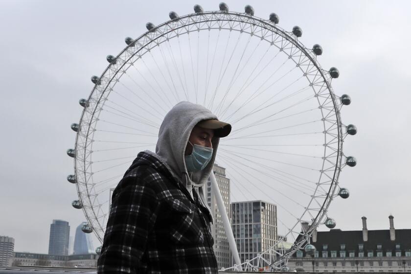 A man wearing a face covering walks past the London Eye in London, Friday, Jan. 8, 2021. Britain's Prime Minister Boris Johnson has ordered a new national lockdown for England which means people will only be able to leave their homes for limited reasons, with measures expected to stay in place until mid-February. (AP Photo/Frank Augstein)