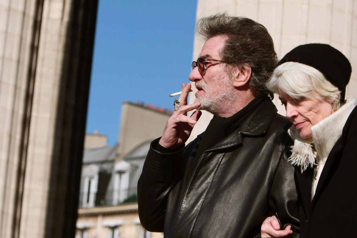 Eddy Mitchell, wearing sunglasses and a black leather jacket, smoking a cigarette next to Françoise Hardy