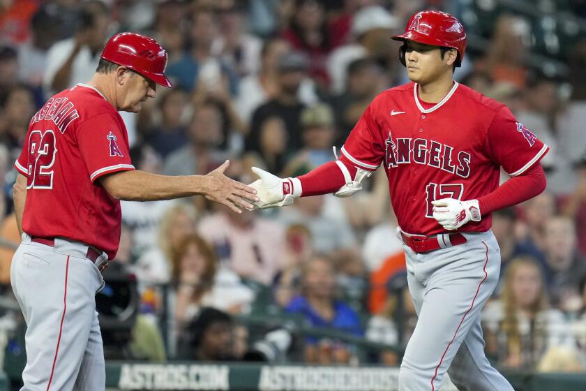 Los Angeles Angels designated hitter Shohei Ohtani, right, clasps hands with third base coach Bill Haselman.