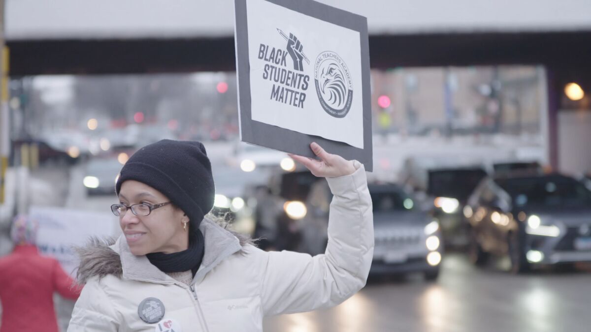 A woman in winter garb holds a sign that says "Black Students Matter in the film "Let the Little Light Shine."