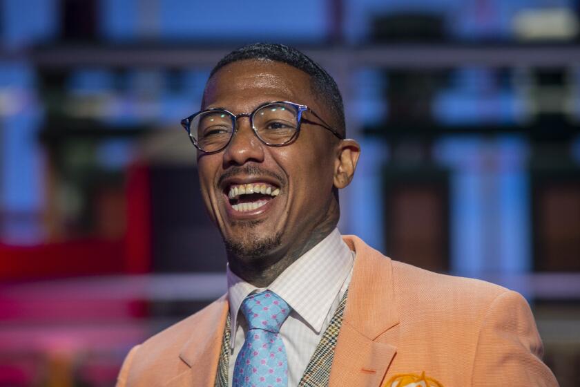 A man with glasses and a burnt orange suit laughs