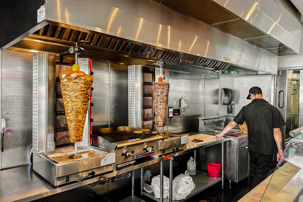 A cook behind the counter at a restaurant that features shawarma spits.