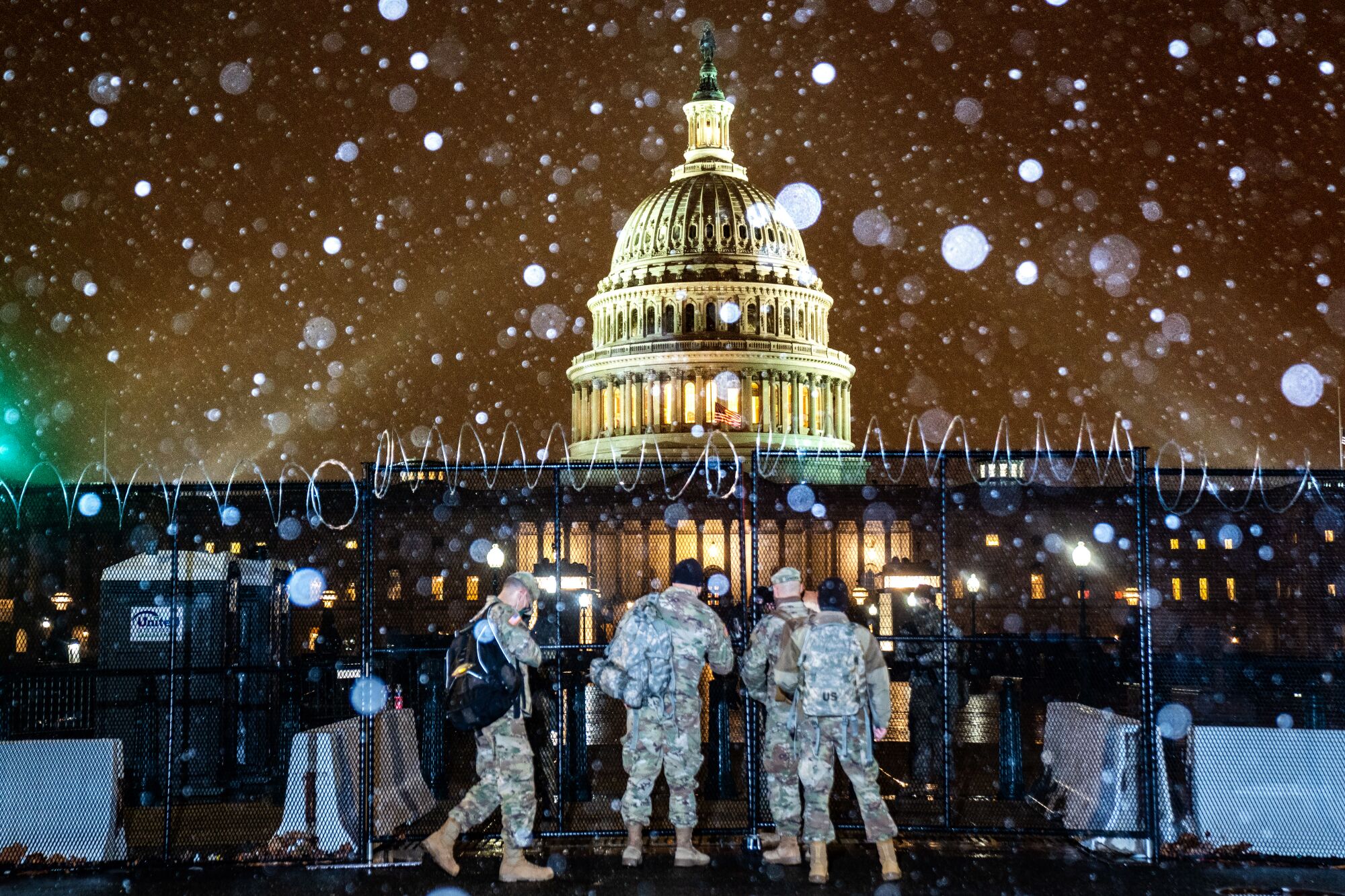 Troops stand outside a gate as snow falls in front of the U.S. Capitol.