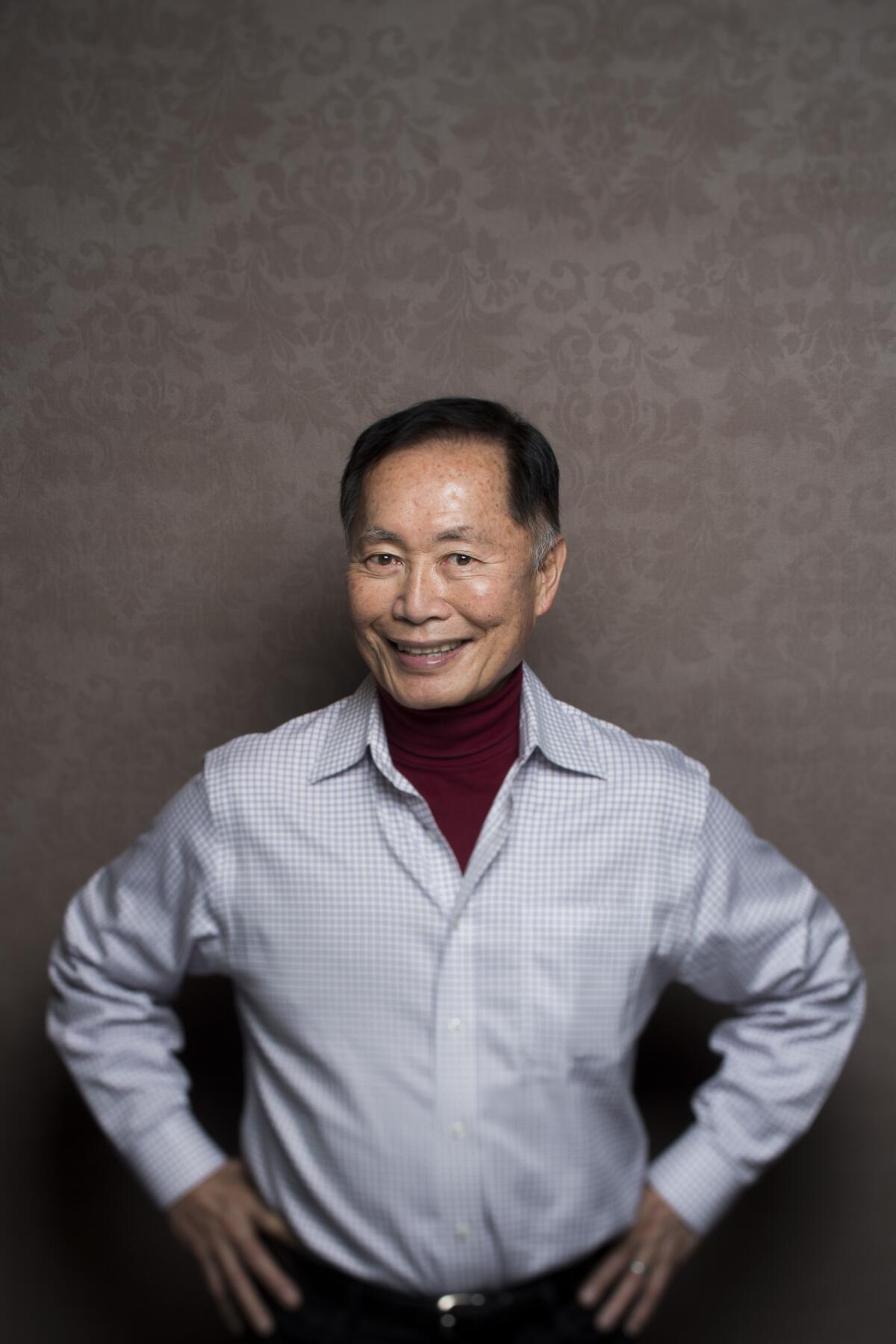 A man in a dress shirt smiles and poses with his hands on his hips