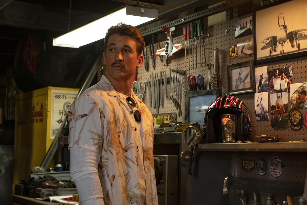 A man in a tropical shirt stands near a wall with tools attached to it