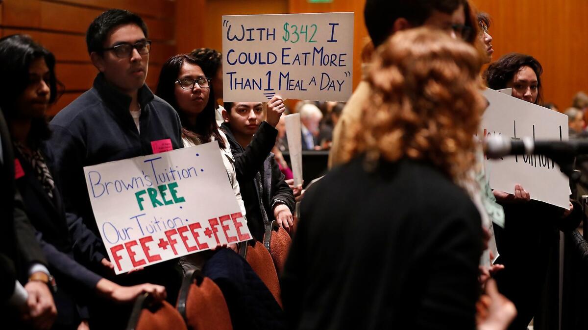 UC Berkeley students Bryan Osario, left, and Angelica Rodriguez, center, hold signs against a tuition hike as another student addresses the UC Board of Regents in San Francisco.