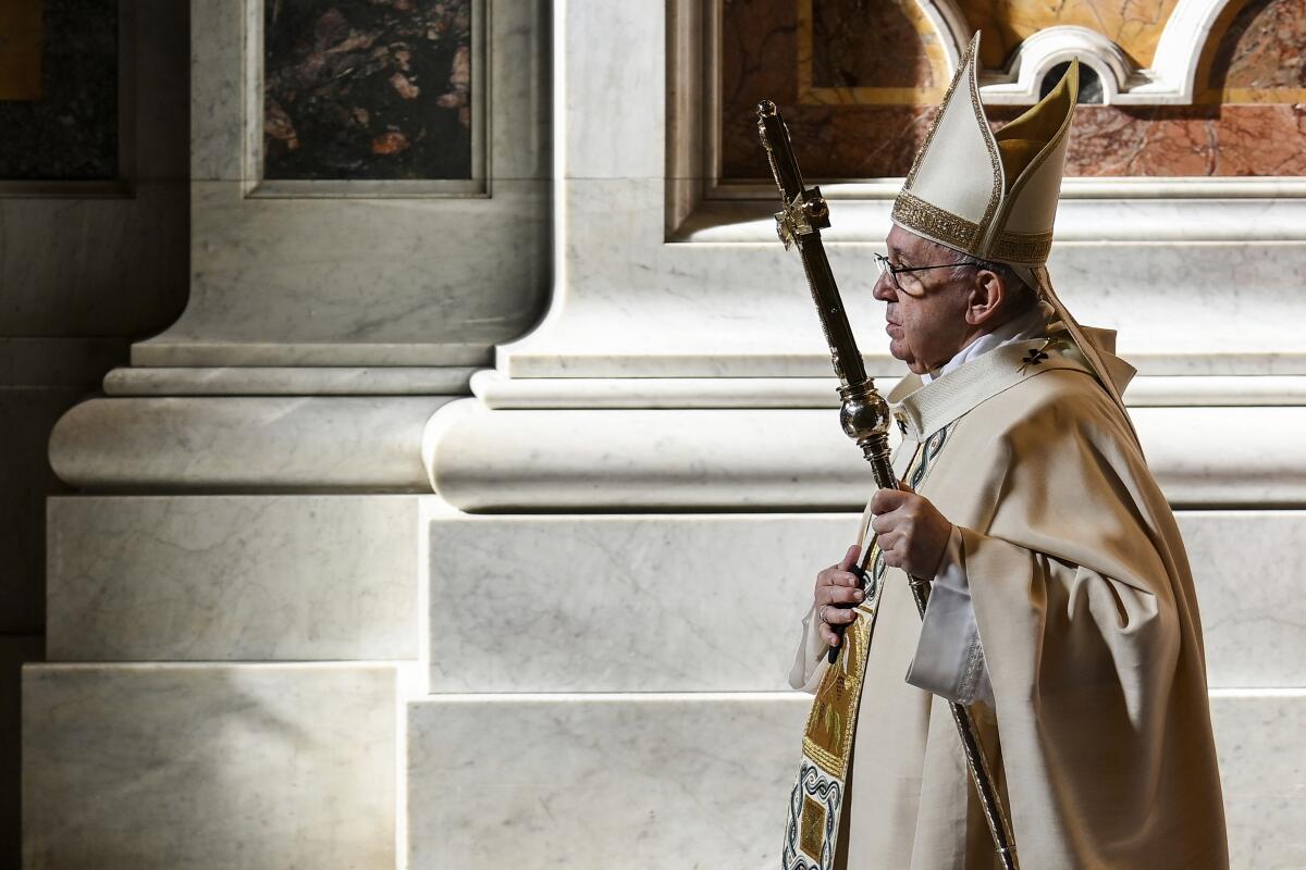 Pope Francis, in robes and mitre, walks by marble columns in the Vatican.  