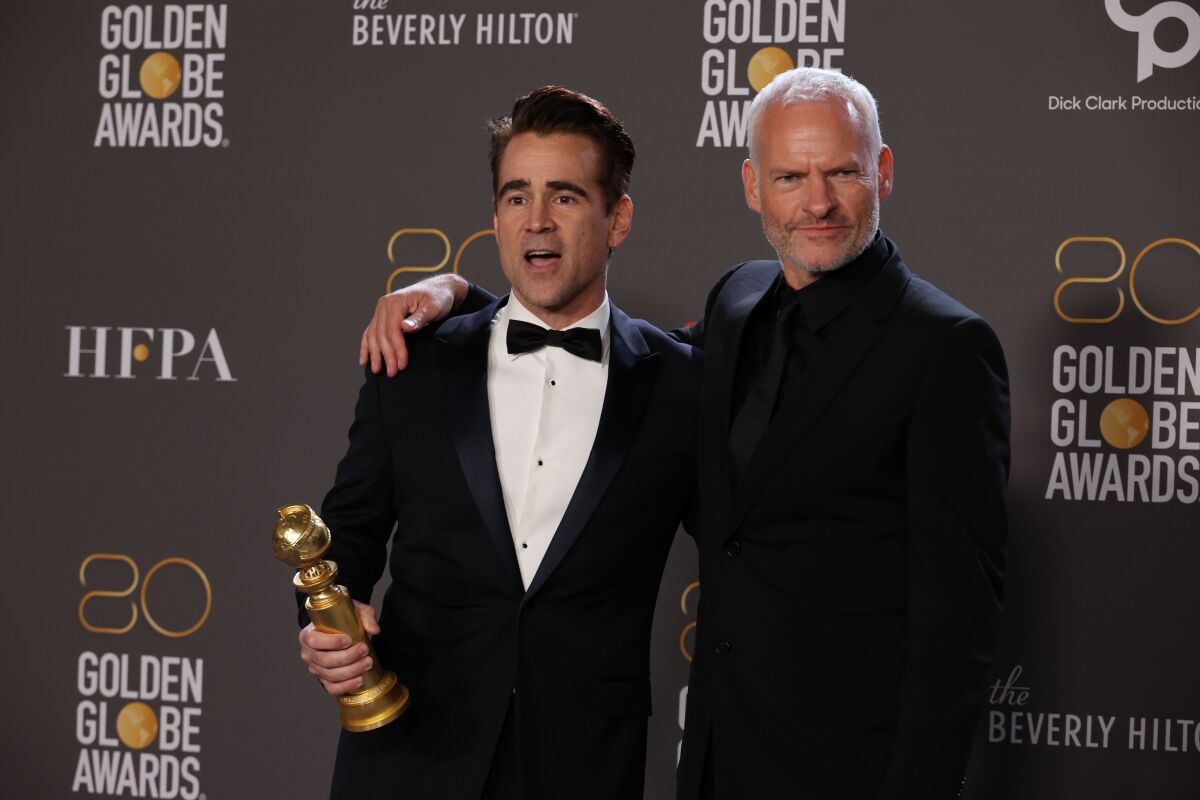 Two men hold a Golden Globe statuette in the awards press room at the Beverly Hilton.