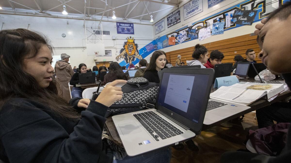 Reseda High School students Jania Garcia, 16, left, and classmate Dennis Miguel, 16, work at signing on to a college prep app on a laptop in the school gym as UTLA teachers are out on strike.