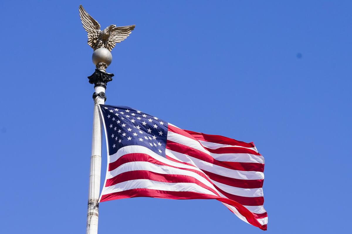 A U.S. flag flies on a flagpole with a metal eagle perched atop it. 