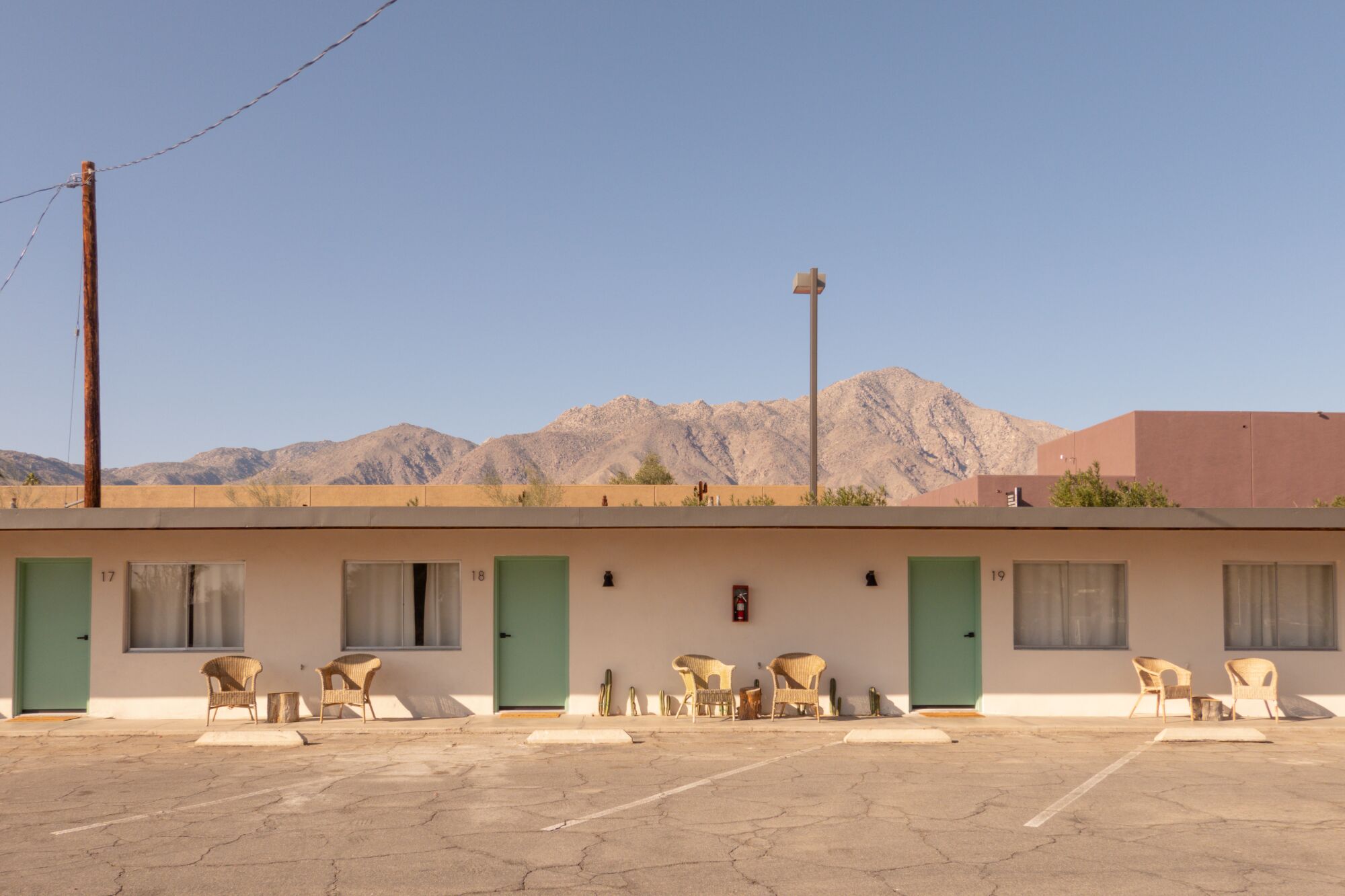 A view of a low-slung motel building with green doors, set against a vista of desert mountains.