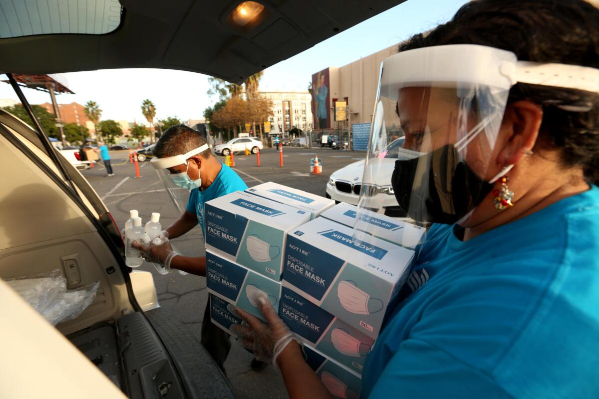 Two people load boxes of masks and hand sanitizer into a car.