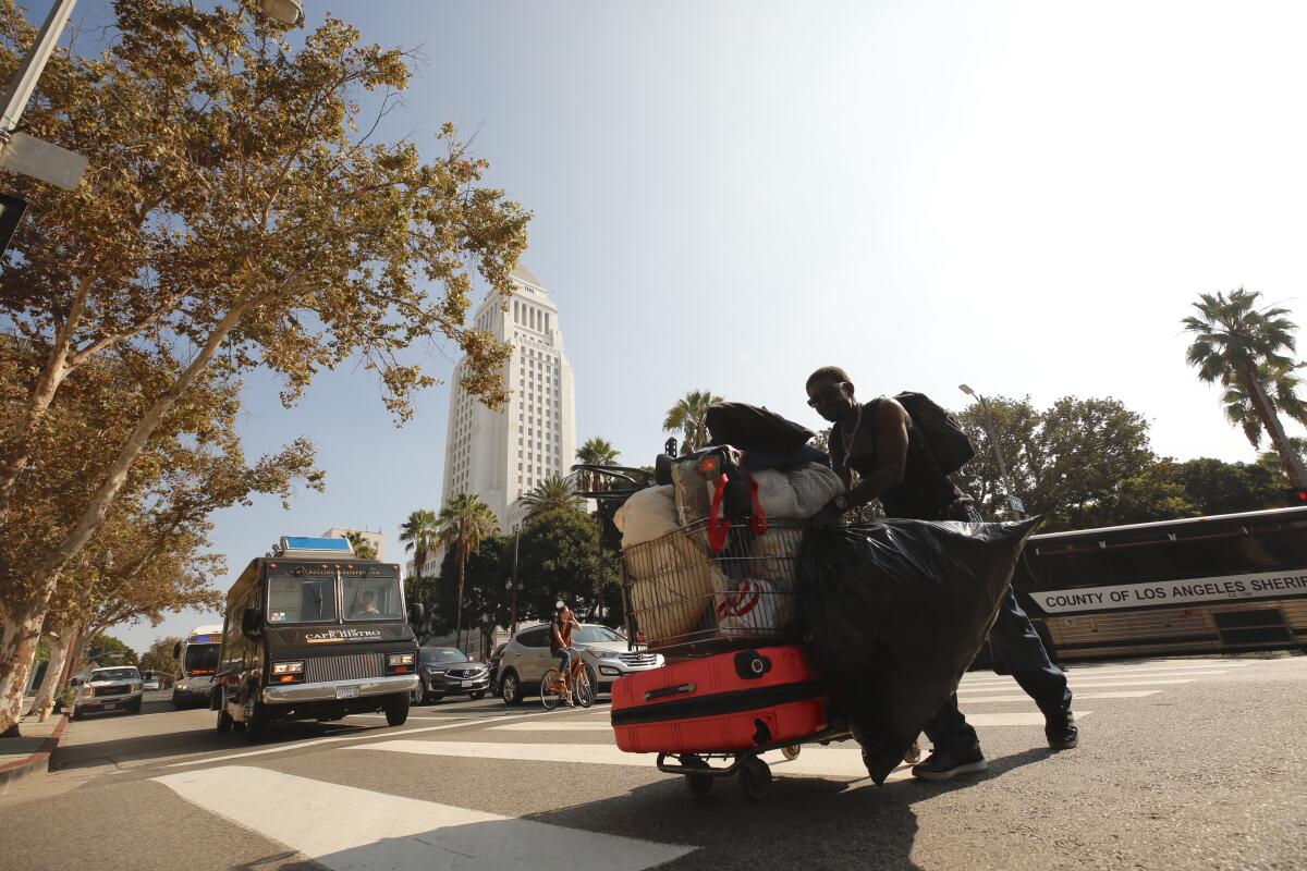 A homeless man pushes a shopping cart in the intersection of First and Spring streets