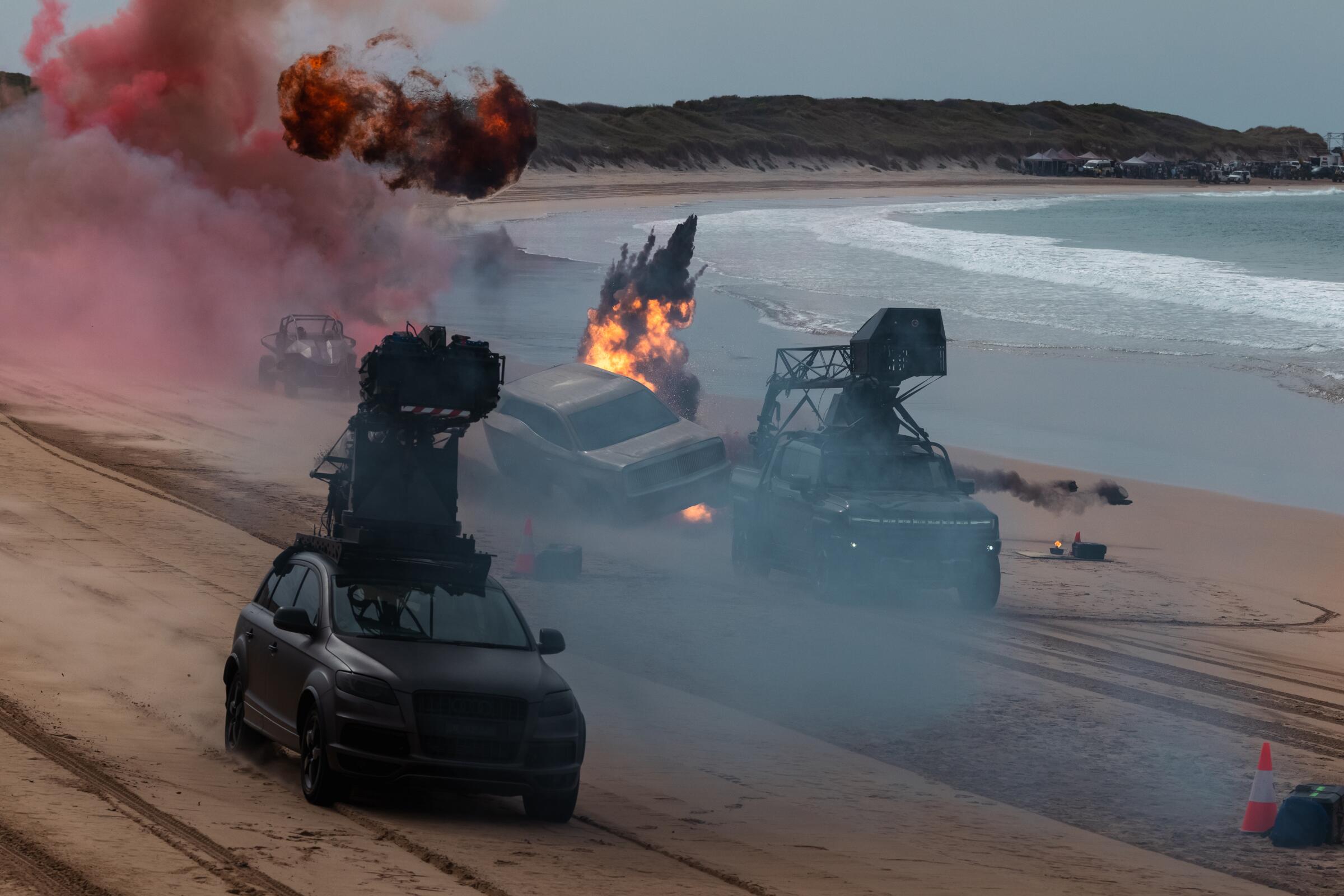 Cars drive through explosions on a curving beach.