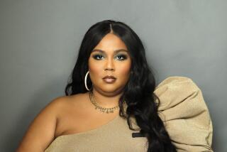 Lizzo looks straight on while wearing a golden one-shoulder blouse and leopard pants