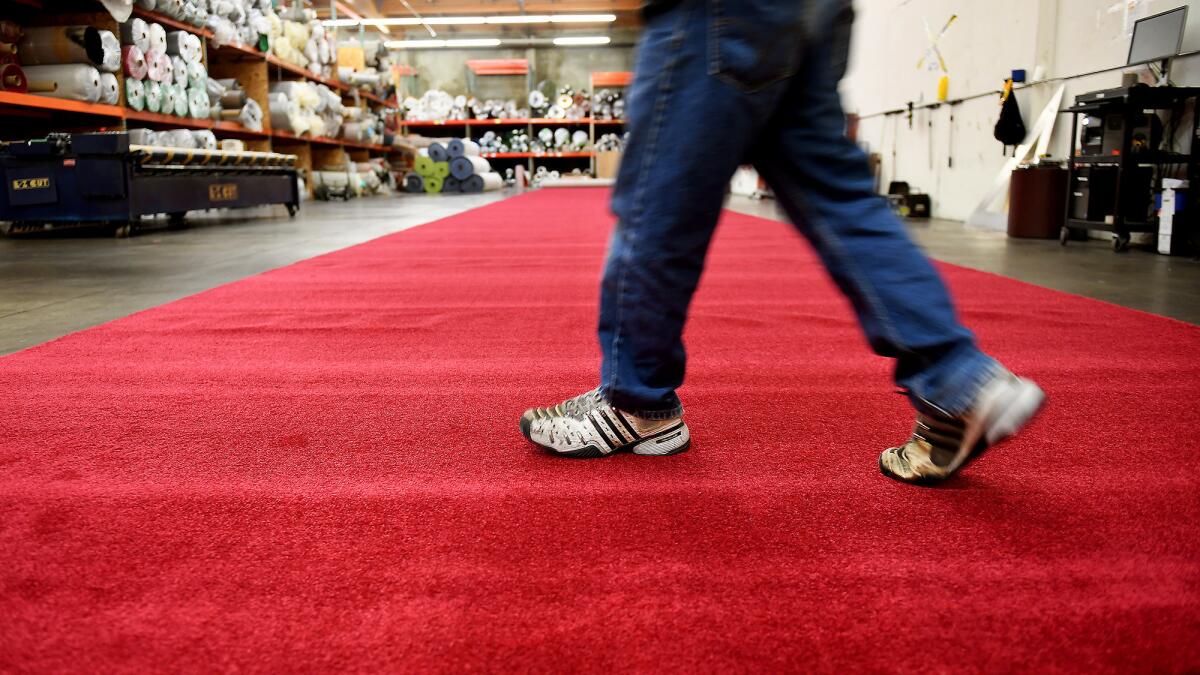 A carpet installer at Signature Systems Group walks across the red carpet in Santa Fe Springs. (Christina House / For The Times)