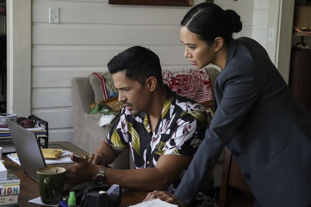 A man in a Hawaiian shirt sits looking at a laptop as a woman in a blazer stands over him in a scene from "Magnum P.I."