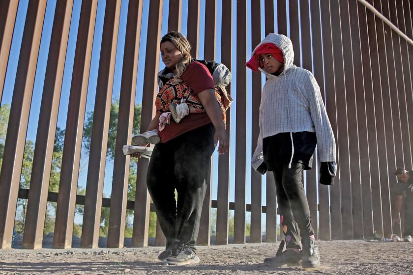 Nigerian Mary Otaiyi, 33, carries her four-year old daughter on her back as her 10-yr. old walks next to her along the border wall in Somerton, Arizona, on Friday, May 5, 2023. Otaiyi, who is seeking asylum in the United States, flew to Brazil where she took multiple buses through Bolivia, Peru and Central America before arriving at this location.