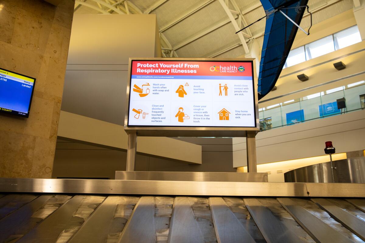 A screen with info on how to "Protect Yourself From Respiratory Illnesses" above an empty baggage carousel.