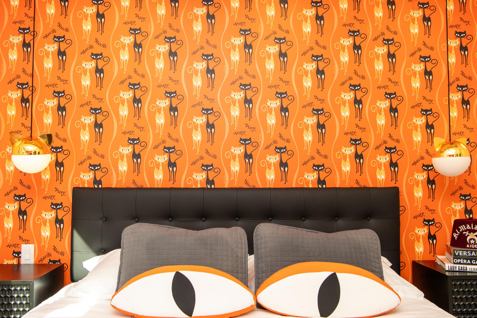 A cat-themed bedroom in the Shag House has cats on the wallpaper and cat-eye pillows on the bed.
