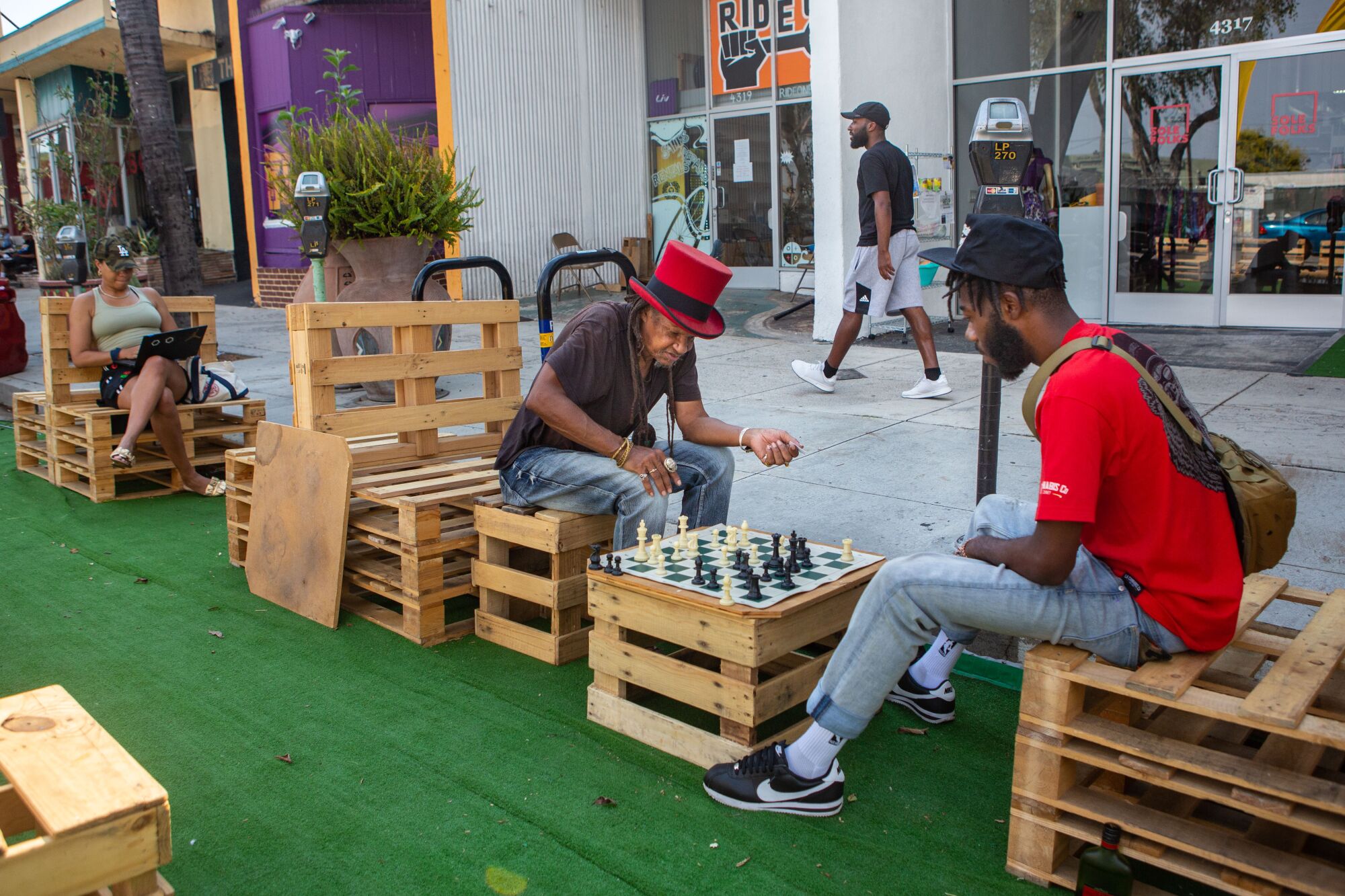 Two people play chess on wooden furniture set up on the street