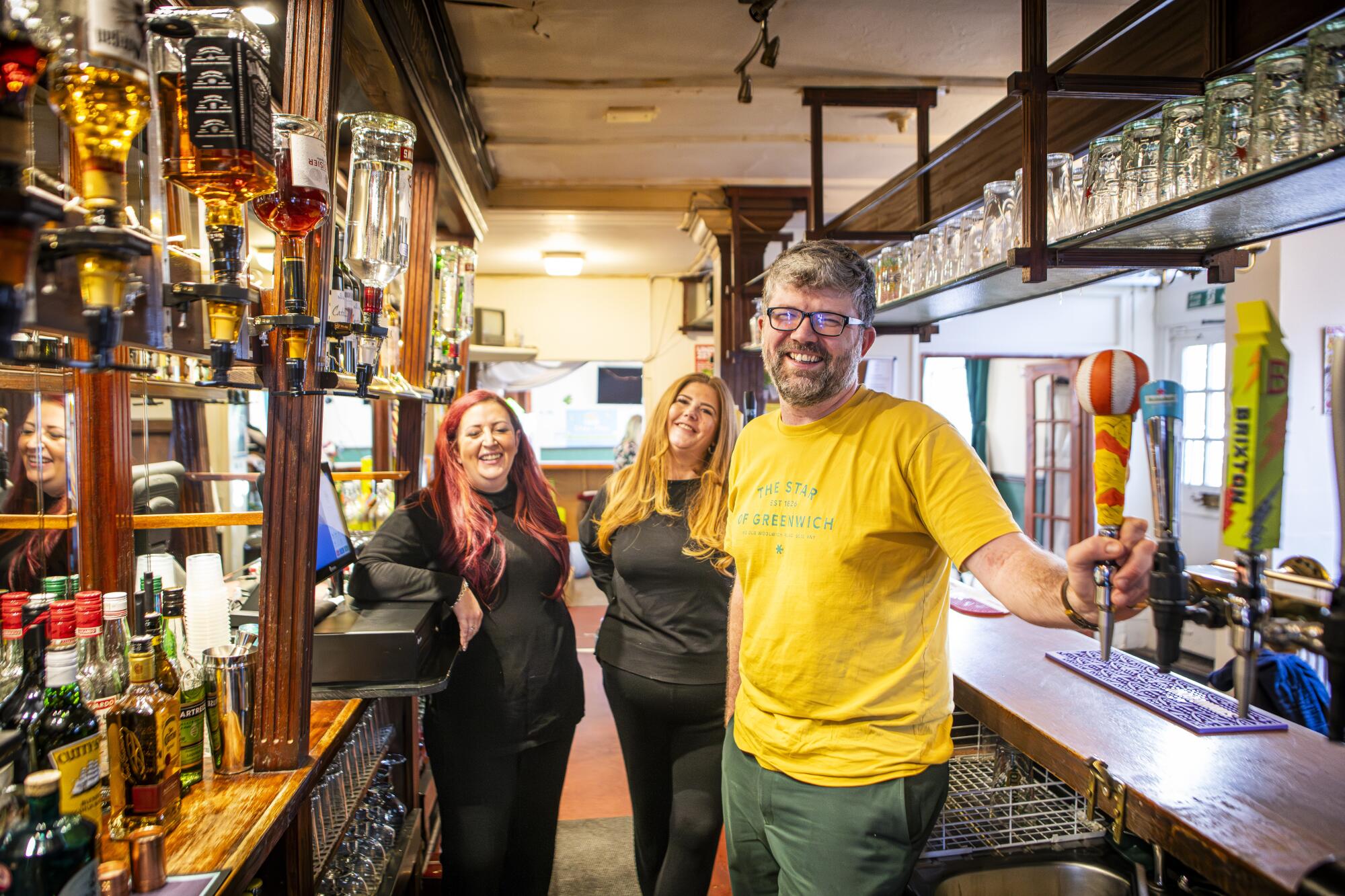A man and two women stand behind a bar 