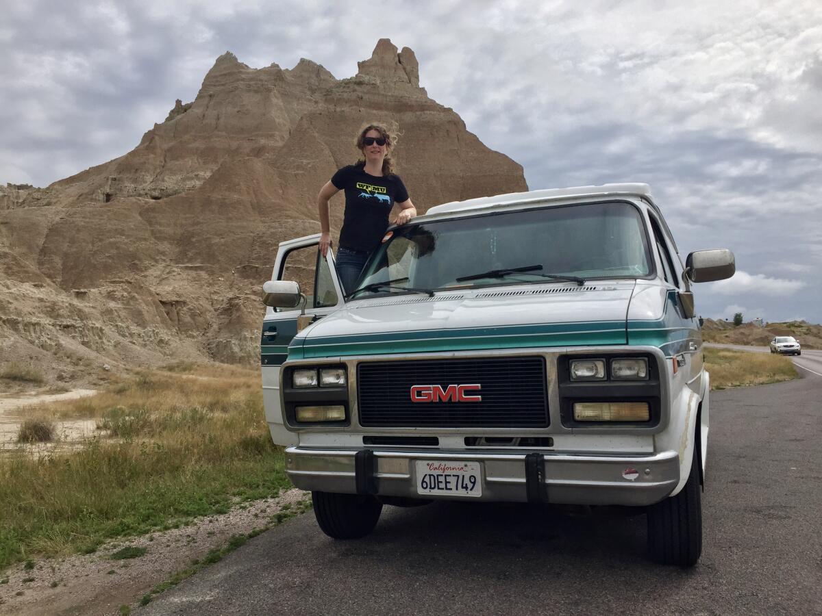 Author Jessica Bruder stands on the door sill of a GMC van, with mountains behind her.