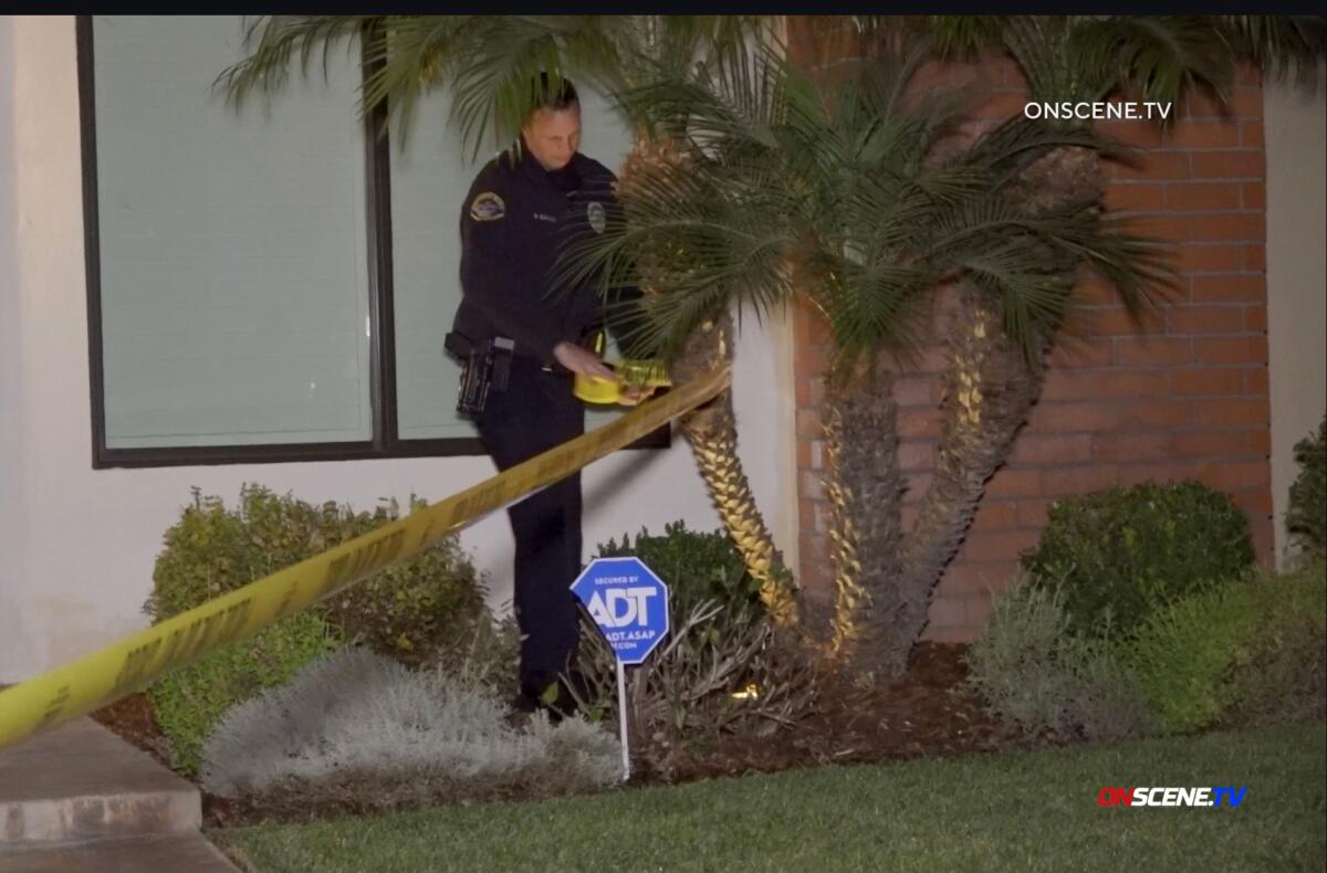 A person in a police uniform puts yellow tape around a palm tree.