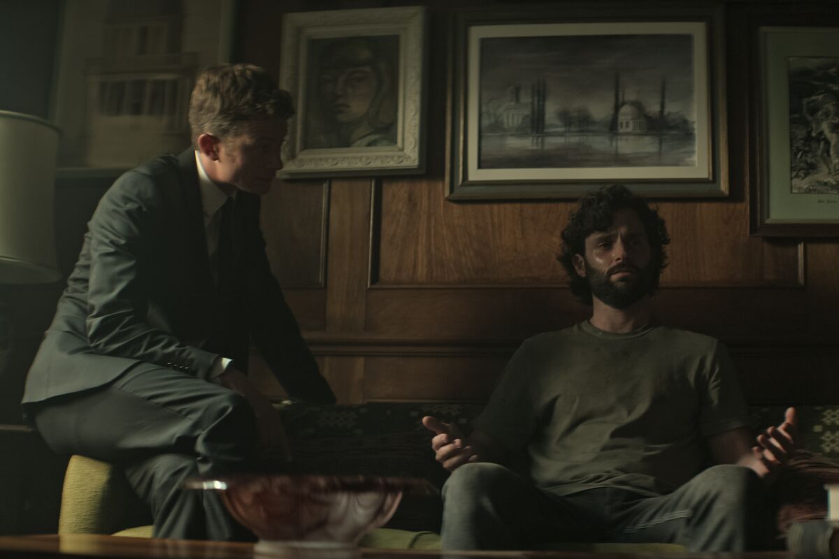 Two men sit in a dimly lighted room.