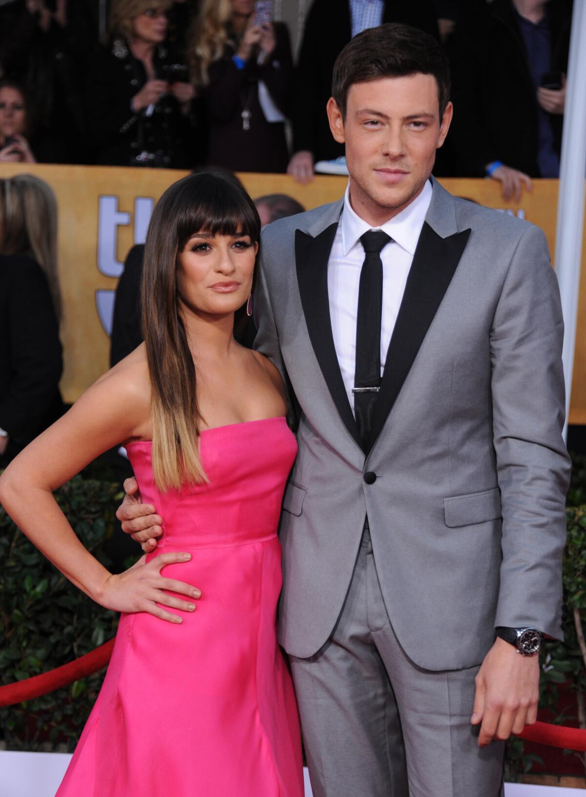 Lea Michele, in a pink strapless dress, stands next to Cory Monteith, who is in a gray suit with black trim