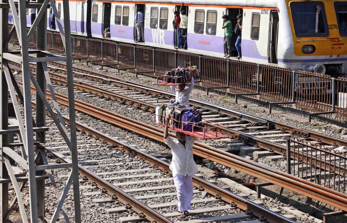 Dabbawalas, or lunchbox delivery men, walk across railway tracks in Mumbai, India
