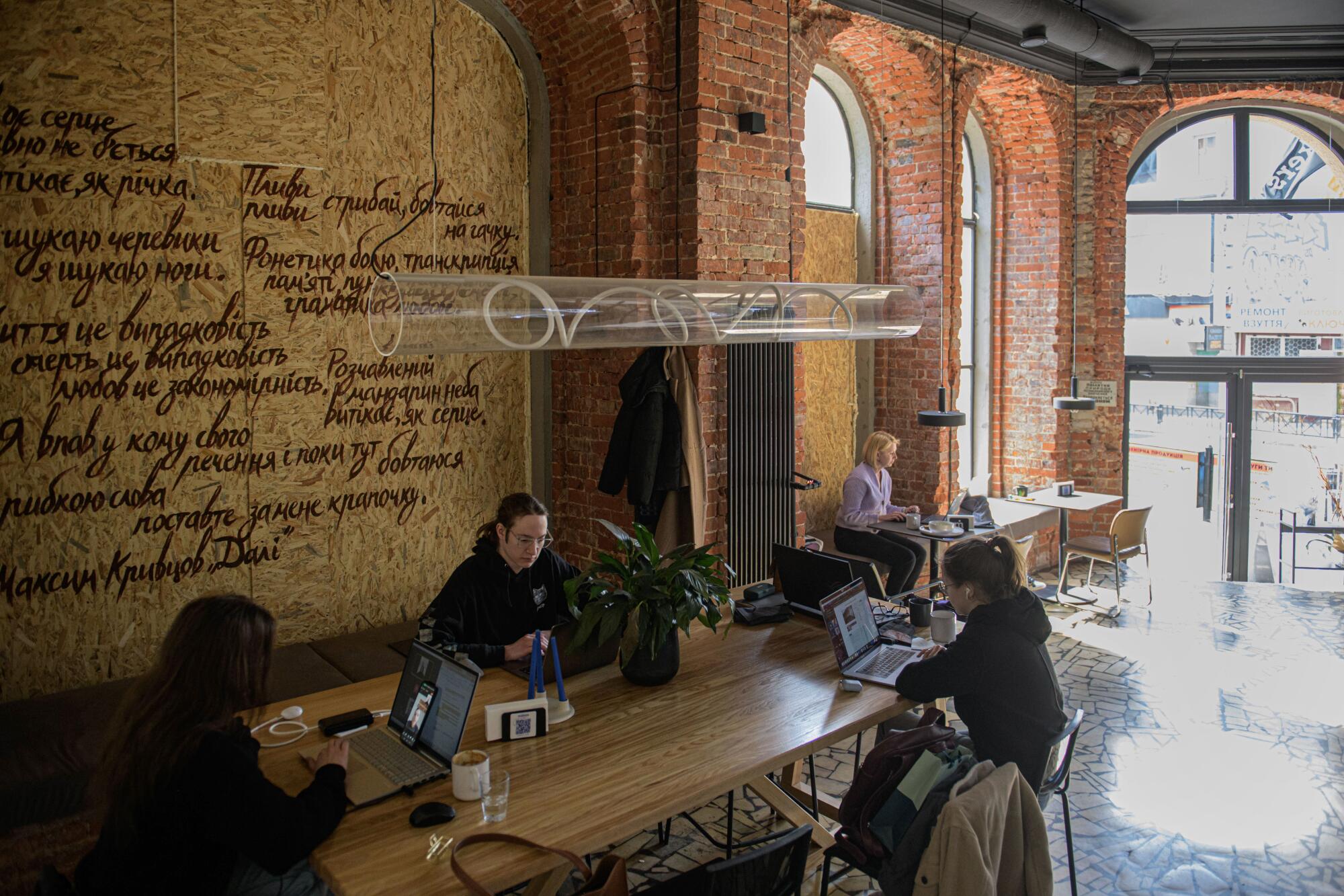 人们在一家窗户用木板封住的咖啡馆里用笔记本电脑工作，阳光从其他门窗照射进来。