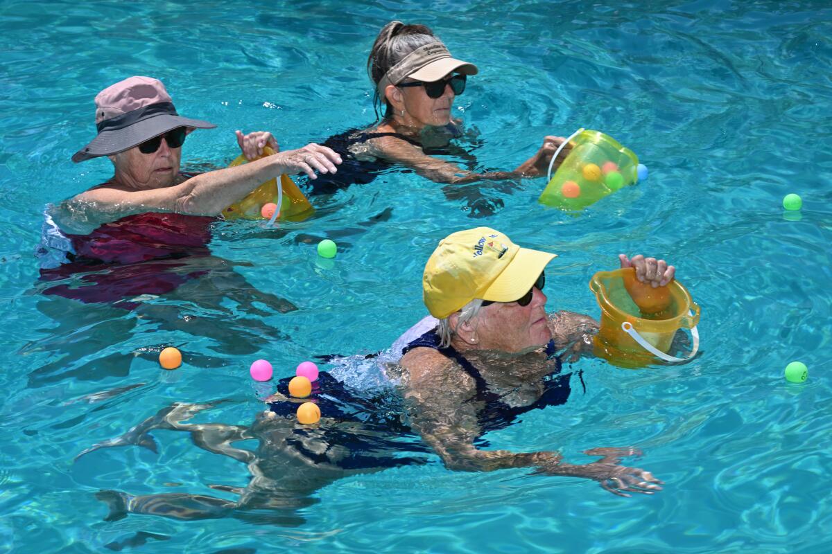 Marilyn Wright, Patricia Peterson and Laurie Teixeira collect ping-pong balls in the water.