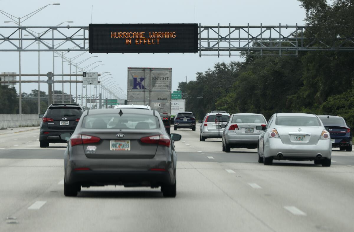 Cars drive past a sign warning of weather on Interstate 95 near Boynton Beach, Fla., as the storm Isaias approaches.